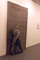 Sculpture of person with vertical grooves walking next to wall with horizontal grooves