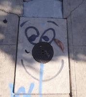 Cartoon face drawn on sidewalk with access hole cover as nose