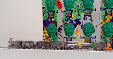 Foreground: silver toy train cars; background: painting with green faces with bulging eyes and slightly protruding tongue