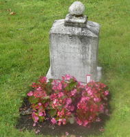 Weathered headstone with red flowers at base