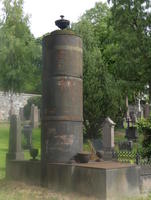 Tall cylindrical metal grave marker with urn on top