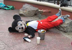 Man in Mickey Mouse suit, lying down with vodak bottle in hand.