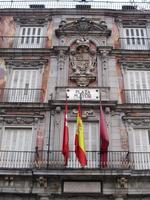 Detail of building in Plaza Mayor, with three flags beneath heraldic emblem.