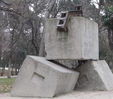 Large sculpture with two stone blocks on bottom, one on top, and a bent metal bar on top.