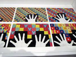 Book page with panels. Each panel shows a hand or hands holding up a certain number of fingers; the background is tiled with blocks spelling the number