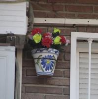 Flowerpot painted with a blue flower; it holds red and yellow flowers