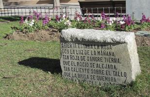 Rectangular stone with Spanish poem; flower bed in background