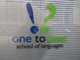 Sign for “one to one school of languages” showing an exclamation point and question mark, with faces for the dots, talking to one another.