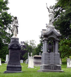 At left, grave with statue of angel; at right, statue of woman with raised fist
