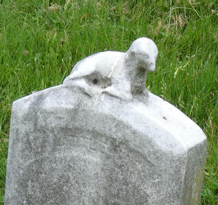 Faded headstone with what appears to be a small seal (aquatic mammal) on top