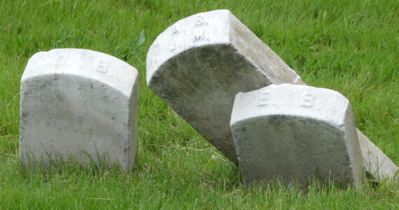 Three headstones tilted over and leaning on each other