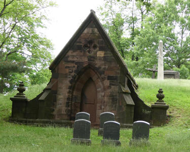 Brick mausoleum with peaked roof; five headstones in front