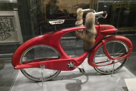 Red bicycle with raccoon tails on handlebars