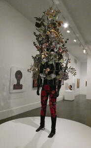Statue of man in red and black pants with flowers growing around a cage over the head