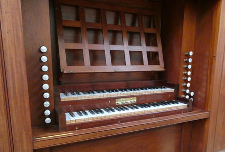 Two keyboards on pipe organ; to right and left are sevral knobs that pull out or push in.
