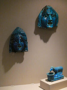 Two blue ceramic masks  and sculpture of sheep drinking water