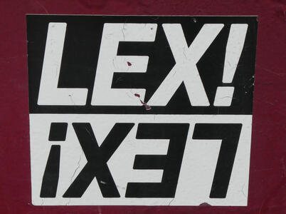 Top half of sticker has LEX! in white on black; bottom half has upside-down LEX! (reading right to left) in black on white