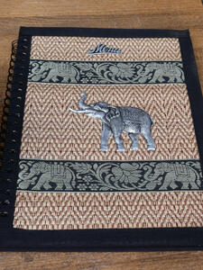 Menu for Thai restaurant with cloth strips on cover, and a silver metal elephant on top of the cloth