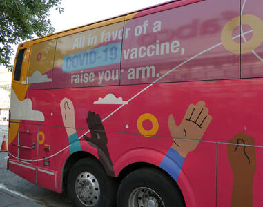 Bus with painting of people’s hands and text: All in favor of a COVID-19 vaccine, raise your arm.