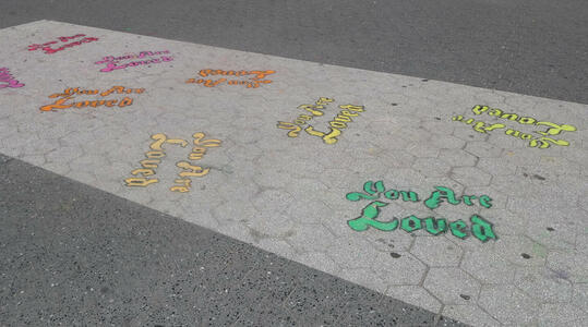 Pavement with ”You are loved” spray painted in many colors at many angles