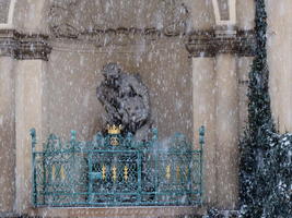 Snowfall in front of statue and blue railing with gold highlights
