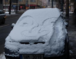 Eyes and nose drawn in the snow covering a car's windshield and hood.