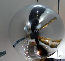 Large reflective sphere hanging from ceiliing in museum.
