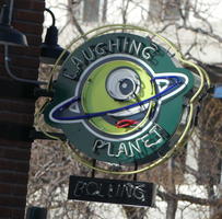 Neon sign for “Laughing Planet” restaurant showing Saturn with a smile