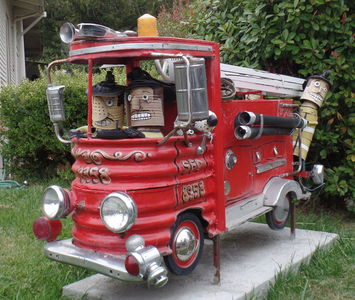 Red fire engine with two people in front and fireman hanging on at the back.