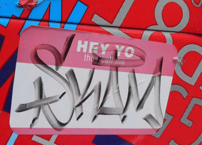 Sticker of a name tag with text “HEY YO / they call me” and SKAM written in graffiti style in the name area.
