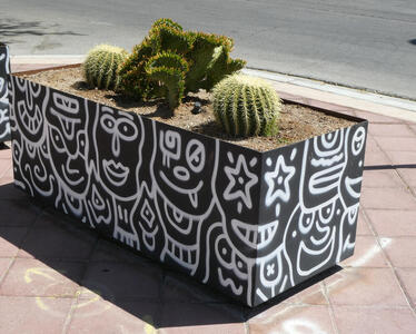 Black planter with line-drawn faces in white; cacti in planter.