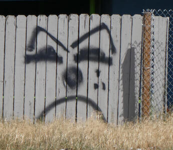 frowning face spray painted on fence