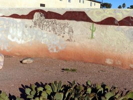 Wall painting of conestoga wagon going through desert w. single cactus; real cacti in foreground.