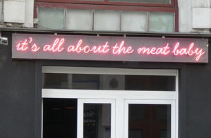Neon sign in lower case cursive: it’s all about the meat baby