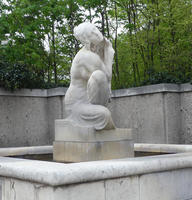 White stone statue of woman in kneeling position, touching her hair.