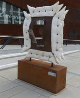 Square sculpture with what looks like white pillows around the sides.
