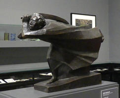 Sculpture of man bent over, walking forward with scythe over his shoulder