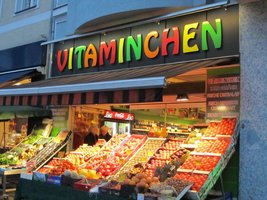 Multicolored “Vitaminchen” sign above fruit and vegetable store; fruit and vegetables on display outside storefront.