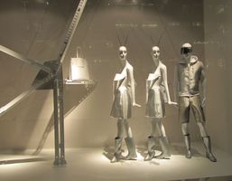 Mannequins in futuristic silver outfits; two women with antenna on heads, man in suit with goggles.