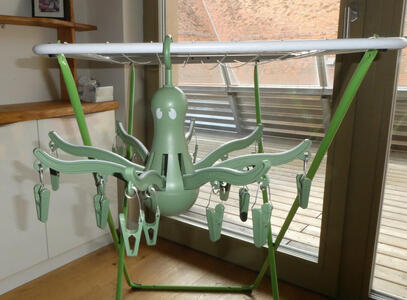 Green plastic “octopus” with eight arms, each having two clips for hanging clothes to dry.