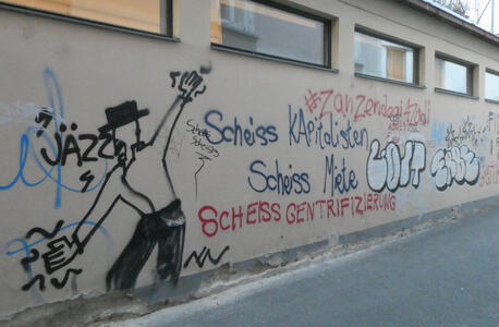 Graffiti of dancing man with hat. Text on wall reads Shit on Capitalists, Shit on Rent, Shit on gentrification.