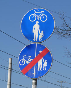 Upper part: bicycle symbol above pedestrians. Lower part: Bicycle symbol on left and pedestrians on right with red diagonal slash.