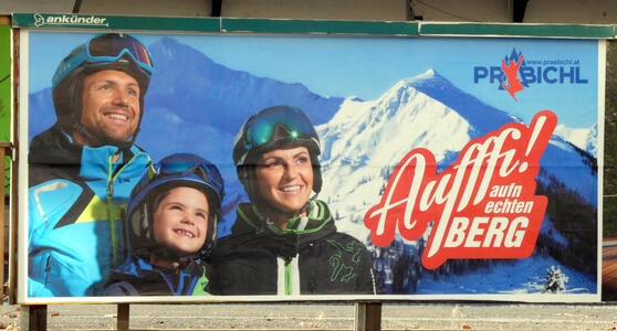 Billboard for ski vacation showing smiling man, woman, and child in ski clothing.