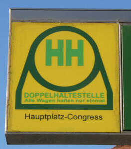 Sign with two green letter H  in green circle on yellow background. Doppelhaltestelle / Alle Wagen halten nur einmal