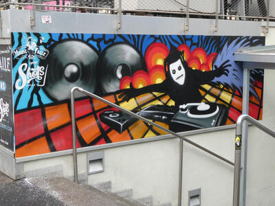 Spray-painted drawing of a DJ in black clothing with white mask