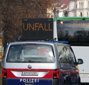 Portable LED sign reading UNFALL (accident); police car in foreground