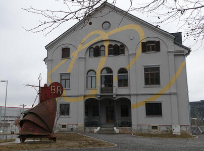 Building with yellow curvy line painted on front. A rusty metal sculpture in the shape of a cornucopia is in front.