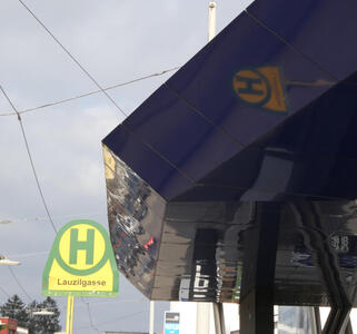 Tram stop sign reflected in the roof of a nearby building