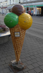 3-d display: Large waffle cone with three different colored scoops of ice cream, in front of gelateria and crepe restaurant