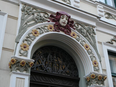 Reliefwork on arch above door. Woman has red hair, and there are yellow flowers on the arch.